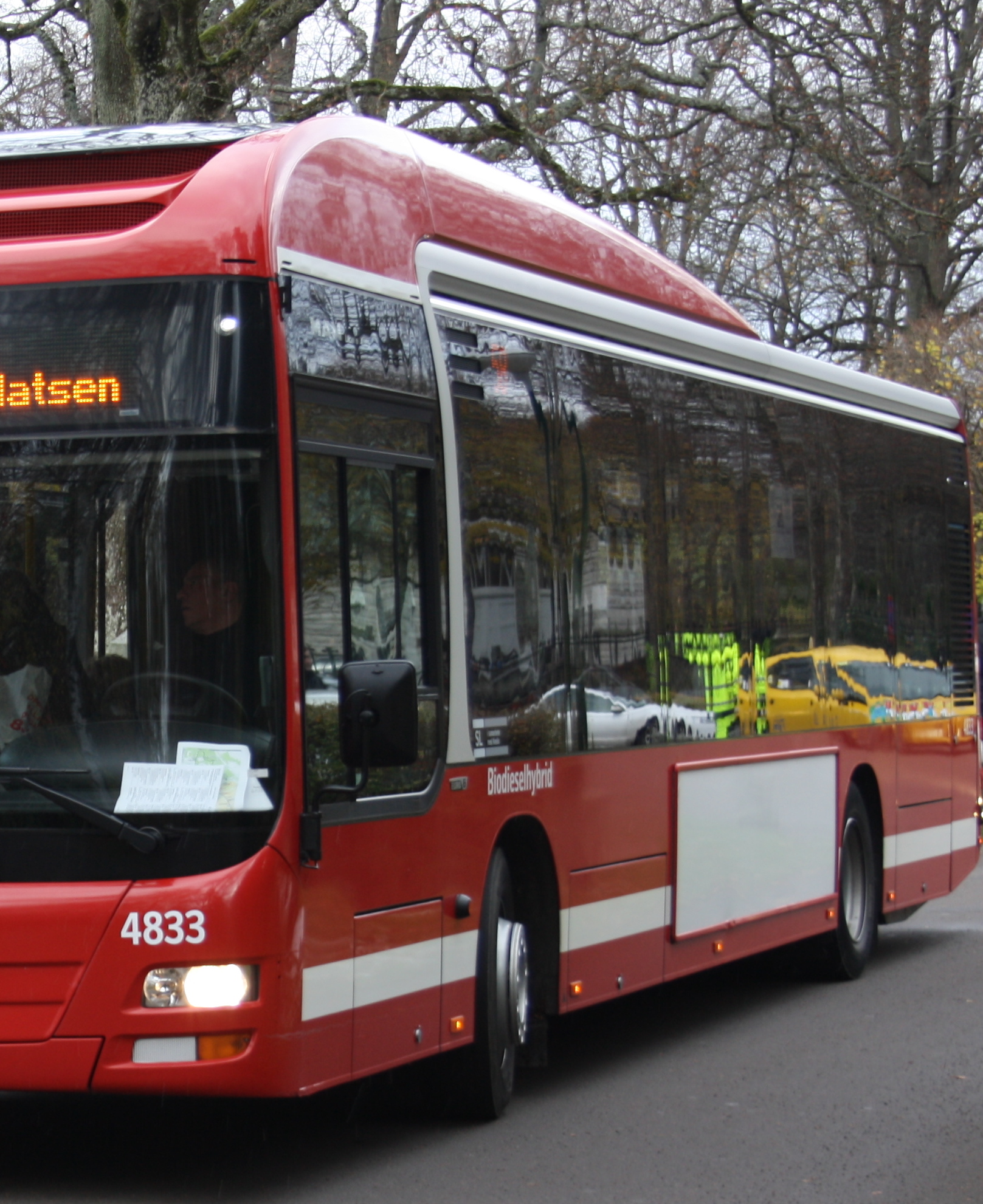 Syntolkning:
Röd stadsbuss, i bussens fönster speglas bilar och hus. 
