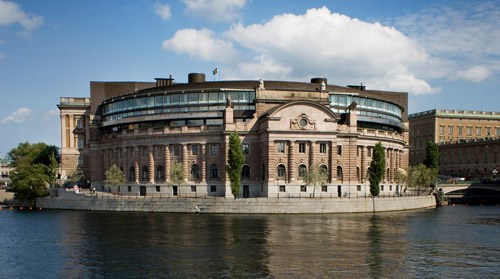 Riksdagshuset mot vattnet en solig sommardag.