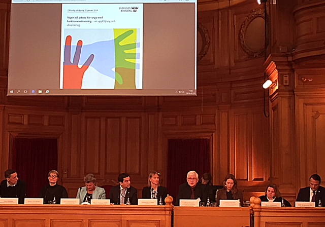 På bilden syns personer på rad på podiet i riksdagens träpanelklädda Andrakammarsal. Från vänster i bild Lars Ahlenius, Stockholms stad, Jessica Arvidsson, Högskolan i Halmstad, Ylva Johansson, arbetsmarknadsminister, Marco Venegas (MP), Madeleine Nyman utredare, Bengt Eklund Arbetsförmedlingen, Annica Nilsson Riksförbundet Attention, jag Maria Johansson Lika Unika, Erik Andersson (M).